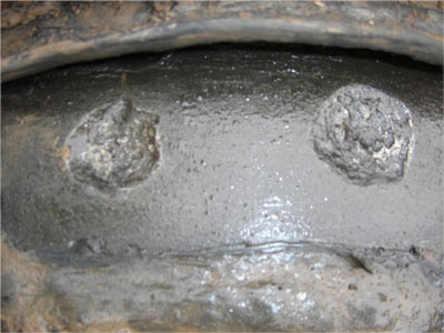 This image shows a closeup of AC interference induced corrosion, which appears as round craters in the pipeline coating.